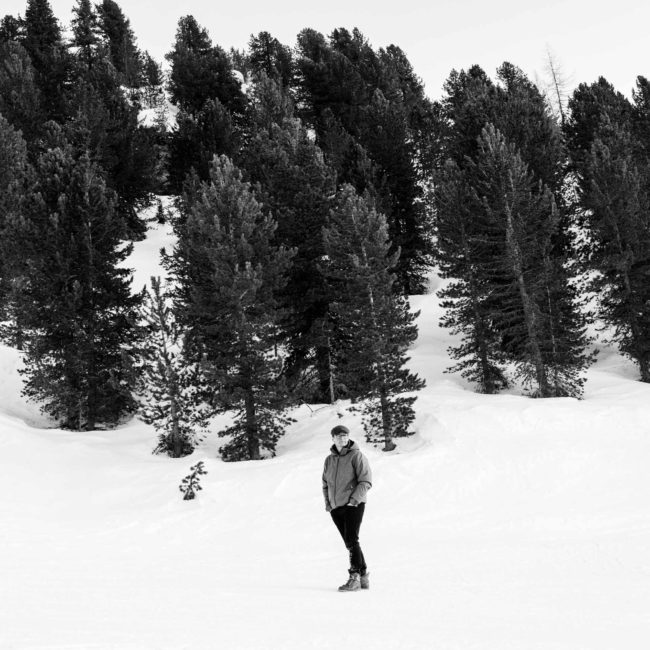 Sort/hvid portræt af Anders Langballe, der står i den hvide sne foran store træer.