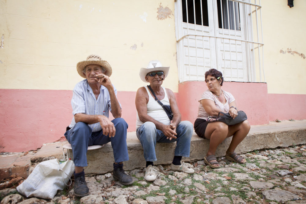 Local older people wearing hats, sitting in the sidewalk on a coppelstoned street in Trinidad, Cuba